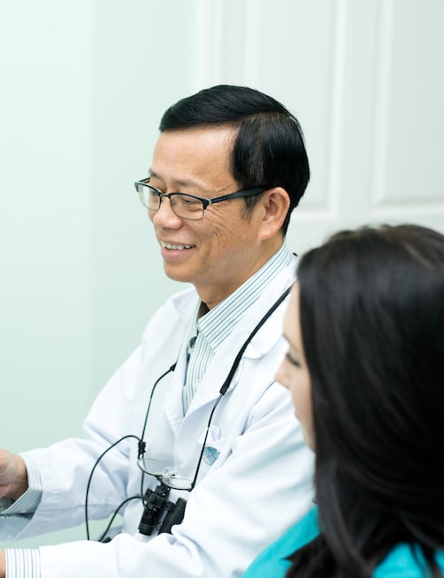 Our friendly Dr. Tan Binh Nguyen smiling sitting next to his dental assistant